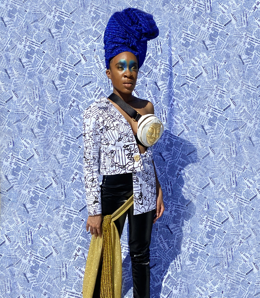 Woman in shimmer blue turban. Abstract black and white print asymmetrical blazer. Black faux leather pants with golden glitter waist sash. Newsprint backdrop. Golden mask fanny pack accessory. Dramatic blue eyeshadow on inner eye lid and inner eyebrows.