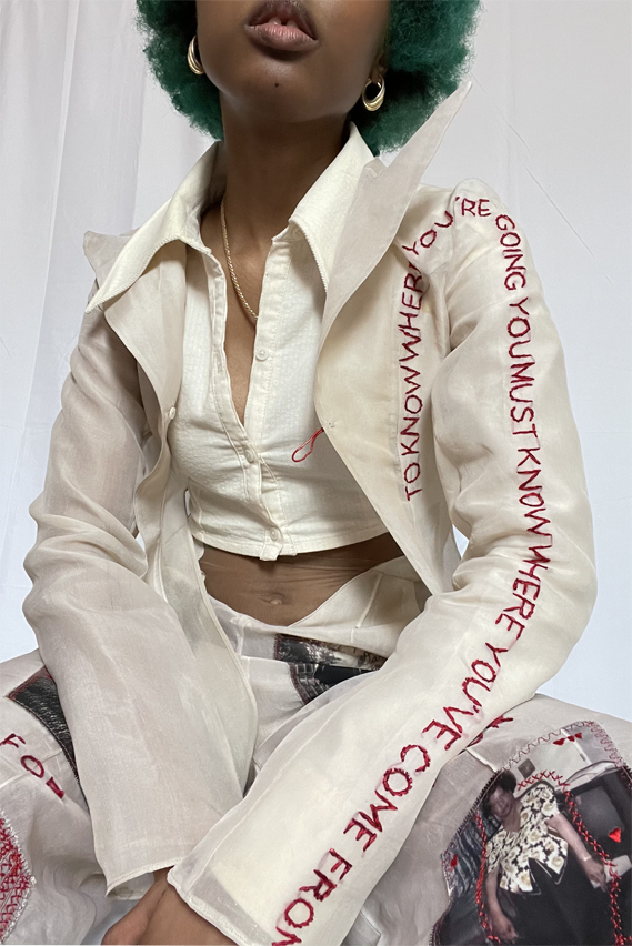 Detail photo. Beige chiffon blazer with hand embroidery stating "To know where you're going you must know where you've come from." 
