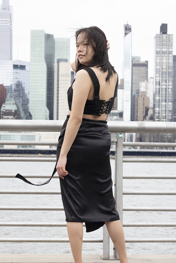 Sleeveless black cropped top with straps, corset closure on center back, and silver grommets and black suede cord trim application. Back of the black crepe, back satin midi wrap skirt, shows the two back darts and has an invisible side zipper closure.