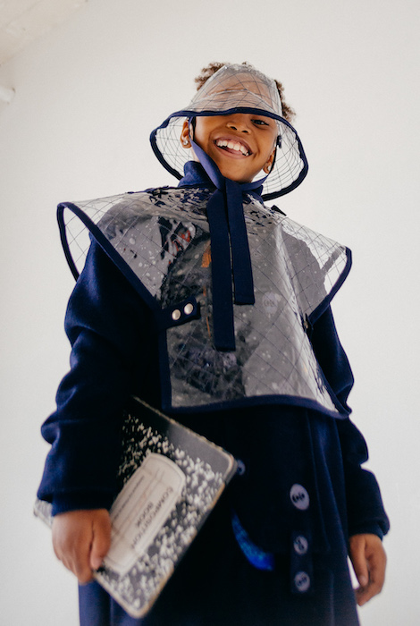 Above is a patched wool navy trench coat with button details. Layered on top is a quilted vinyl poncho and quilted vinyl bucket visor.