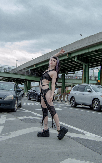 Model standing in the middle of the road, raising her right hand in the air.