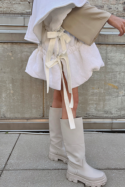 Side view of puffer vest that has long straps that gather throughout the body and come out on the side to tie into a bow