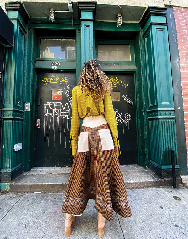 This image displays the back of the look without the jacket and the denim finishes on the wool skirt, such as the yoke, patch pockets, and waistband. The blouse is tucked into the skirt and the background is the same as the previous images.