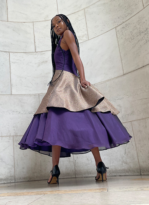 An editorial photo of the plum dress's side view, once again without the cropped jacket. This photo is captured in motion, which displays the fullness of the layered circle skirts as well as how the garment naturally moves when executing any form of motion. The skirts are clean finished with French seams and hemmed with either the baby hem method or hidden with the usage of lining. The bodice creates a chest projection through princess seams and unpadded bra cups for comfort and support.
