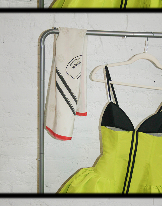A front view close-up of the Surfboard Dress hanging on a rack with the silk scarf reading "Tailored Surf Shop, By Hollis, NY, NY"