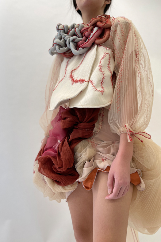 The look is adorned with a neck scarf that is netted with wool yarns wrapped in scraps of fabric.