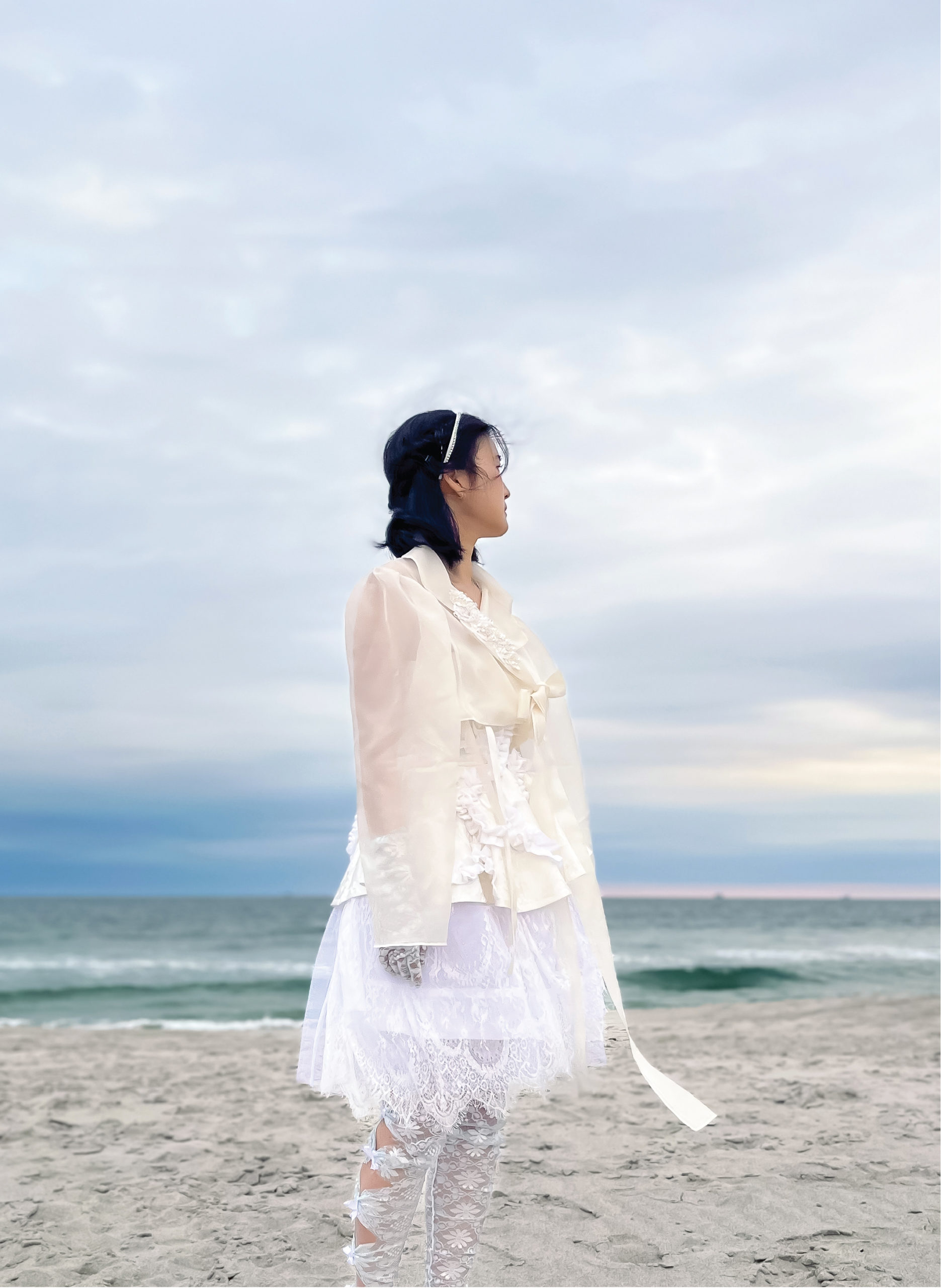Model looks behind into the sky with jacket closed, tiered dress, and cutout leggings with bows.