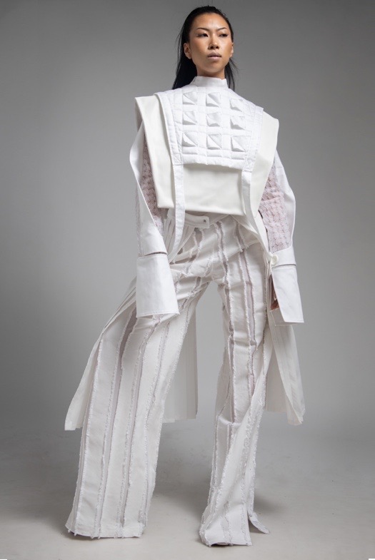 Double-layer vest worn over sheer houndstooth top, abstract striped pants, and pleated belt.