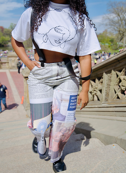 This is a close-up image of the white tee with the painted African-American portrait and newspaper-printed suspenders. The model is walking up the Bethesda Fountain stairs. 
