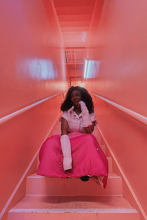 Model, Thalia, is surrounded with pink walls as she poses in thought. 