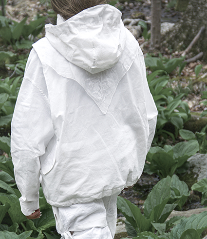Close-up of the white tie pants worn with the green jumbo tie puffer scarf in the woods. The details of the embroidery on the vintage handkerchiefs on the pants are more visible here. The puffer scarf looks like several puffy little pillows tied together at their corners.
