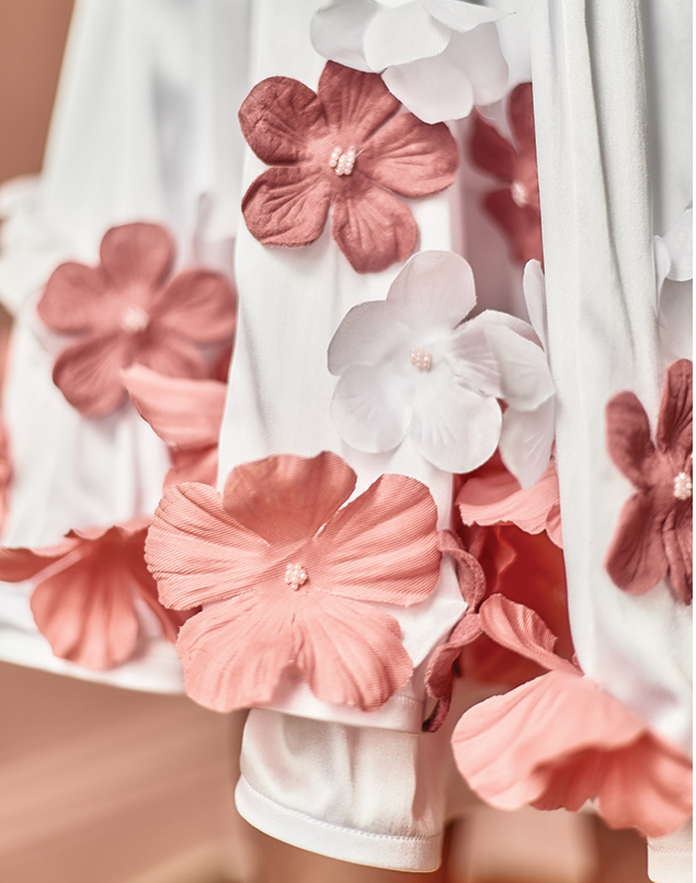 This image is of rose pink, bright pink, and white flowers hand-sewn onto a satin double-layered skirt. This picture shows a close-up of some of the flowers. They flow nicely up from the hem of the skirt. In the center of the flowers, they have small light pink beads that attach it to the dress. It is made of all sustainable fabrications: rose pink Piñatex leather made from pineapple leaves, white recycled polyester satin made from 100% post-consumer rPET recycled plastic water bottles, and white Tencel lining made from wood pulp. 