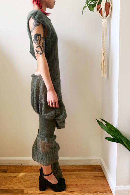 Right view of sage green dress. Showcases a fully fashioned, high-cut seam from the low drop waist to high back cut-out. Tiered skirt drapes dramatically across the front across the thighs and elegantly fluffs around the calves.  