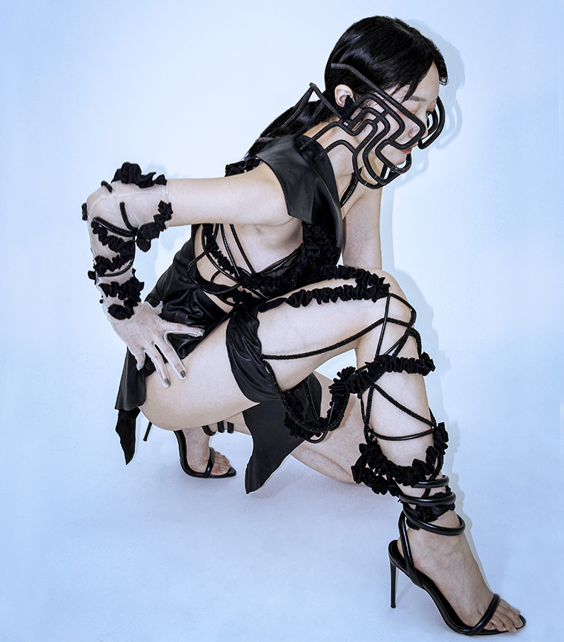 This is a 3/4 view of my garment, model squatting on the ground and showing the detail of my fabric manipulation. You can see all my trims clearly. I use leather cords, black bead cords, and ruffle straps to create a Li tattoo.