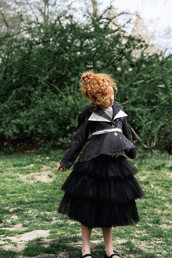 Using denim and texture cotton to create a double-layer collar. The bottom half of the jacket is made into a flare shape. Photo of a little girl standing with her arms open, showing us the details of the jacket.
