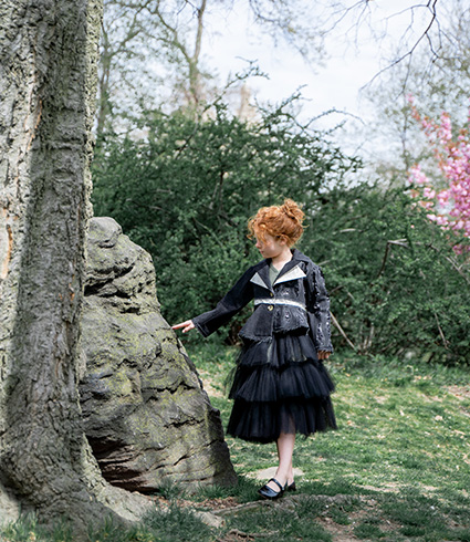The entire look presents an A-shape form. Photo of a little girl touching a rock and playing with nature. 